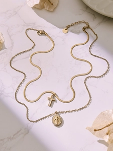 Close-up of golden layered necklaces with cross and Virgin Mary medal on marble