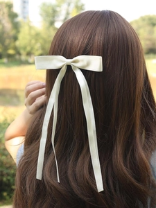 Detail of elegant cream white silk bow hair clip with long ribbons on wavy hair