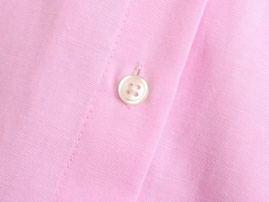 Macro detail of the pink cotton oxford shirt fabric with a white four-hole button