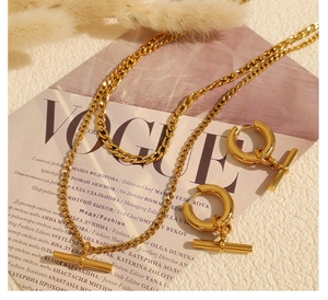 Détail du coffret collier et boucles d'oreilles dorés avec fermoir OT sur fond blanc