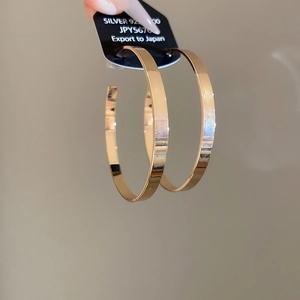 Detail of large gold hoop earrings with silver 925 post on black packaging card