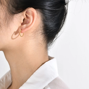 Detailed close-up of a golden twisted rope hoop earring worn by a model on a white background