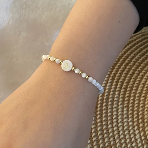 Detail of beaded bracelet with white beads and gold-tone letter S charm on a person's wrist