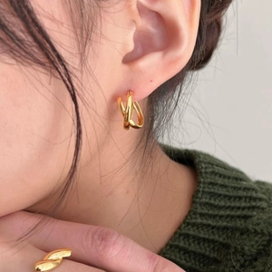 Close-up of a woman wearing gold twisted hoop earrings and a matching ring