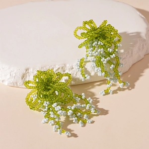 Detail of handmade green and white beaded tassel earrings on natural stone background