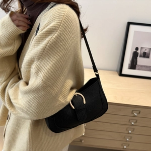 Detail shot of black lychee grain texture and gold metal buckle on a shoulder bag
