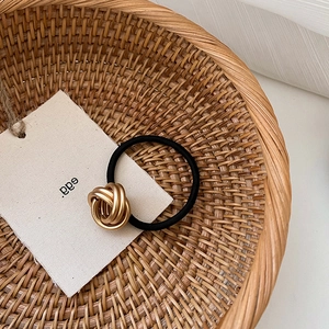 Minimalist black elastic hair tie with three-ring golden braided metal knot in a basket