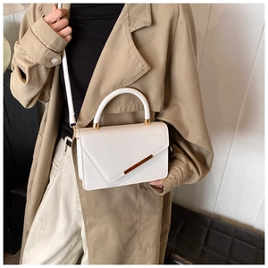Chic white textured leather square bag with gold hardware held by a model in a trench coat
