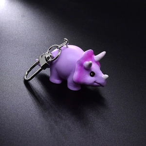 Close-up of a cute purple triceratops dinosaur keychain with a metal ring on a dark background