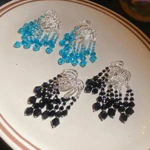 Elegant beaded tassel drop earrings in blue and black colors displayed on a vintage plate