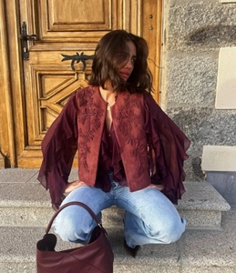 Detailed close-up of ethnic style embroidery on a burgundy vest with ruffled sleeves
