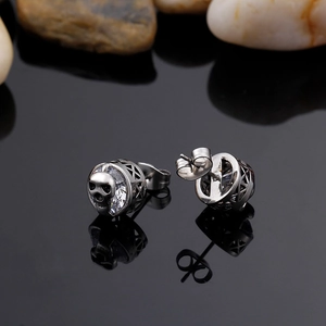 Macro shot of silver skull earrings with crystal inlay on a reflective black surface