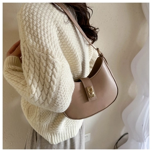 Brown leather crescent shoulder bag with gold buckle worn on a beige knit sweater