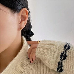 Detail of twisted gold bow stud earrings worn by a model in a cozy knit sweater