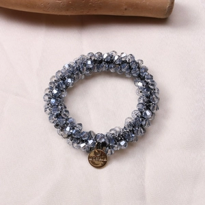 Close-up of sparkling blue faceted crystal hair tie with a gold metal brand pendant