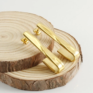 Polished 18k gold hook earrings with twisted metal design on rustic wood base