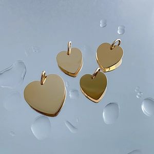 Close-up of polished gold stainless steel heart pendants on water drop background.