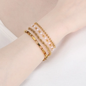 Close-up of a layered golden bracelet set featuring curb, rope, and pearl chains