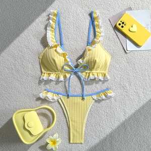 Detailed flat lay of a ribbed yellow bikini featuring white lace trim and blue bow accents