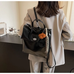 Detail of a large glossy black backpack with a bear charm in a cafe setting