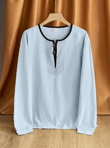 Detail shot of a light blue linen Henry shirt with black collar trim on a wooden hanger