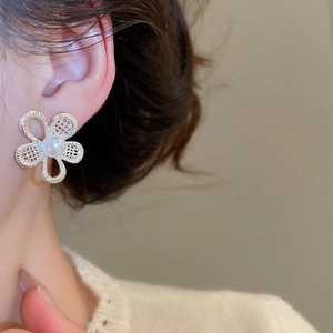 Close-up of elegant hollow flower stud earrings with a white pearl on a model