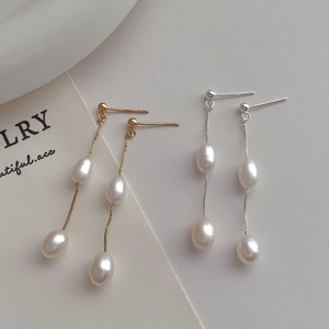 Detail of elegant gold and silver long tassel earrings with white drop-shaped pearls