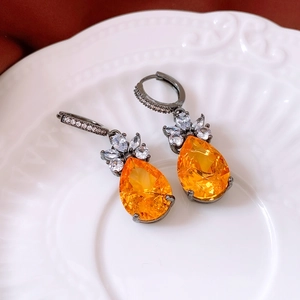 Macro detail of pear-cut orange zircon earrings on a white porcelain dish
