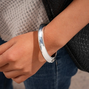Close-up of a chunky silver polished metal bangle on a model's wrist for casual styling