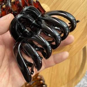 Close-up of a large glossy black pumpkin hair claw clip held in hand for scale