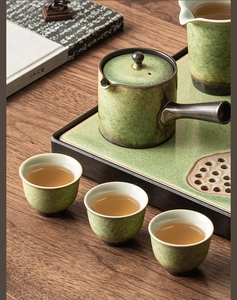 Macro view of green glazed ceramic teapot set with wooden handles on dark wood tabletop