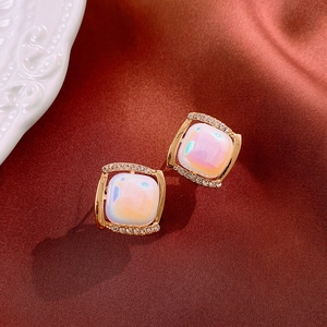 Macro detail of square iridescent stone earrings with diamond accents on silk fabric