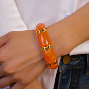 Detail of orange acrylic bamboo-style bangle with gold-tone spacers on a model's wrist