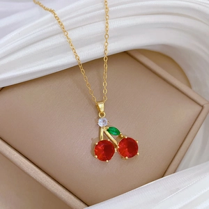 Macro detail of gold cherry necklace pendant with red and green crystal gemstones