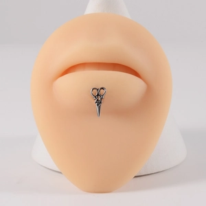 Detailed view of a silver scissors-shaped lip stud on a realistic silicone lip model