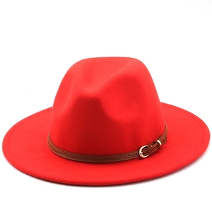 Detail of red wool fedora hat featuring a brown leather band and gold buckle