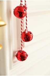 Close-up of three red Christmas bells with star cutouts on a red and white twisted cord