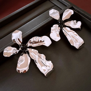 Macro detail of silver flower earrings with pleated metal texture and black center beads