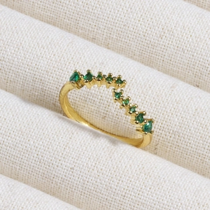 Macro shot of V-shaped gold ring with graduated emerald green zircons on textured fabric