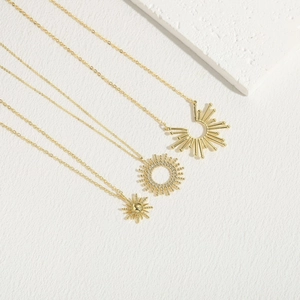 Three elegant 14K gold plated sunflower pendant necklaces on minimalist textured surface