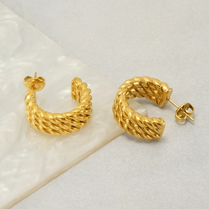 Twisted woven C-shaped gold hoop earrings in stainless steel on marble surface