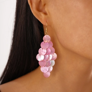 Close-up of pink shell-like round disc tassel earrings on model for beach vacation style