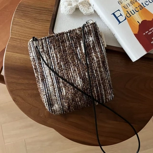 Detailed close-up of textured tweed mini crossbody bag on a warm wooden background