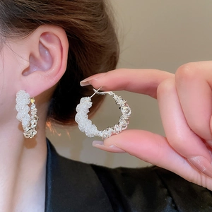 Close-up of twisted woven design silver hoop earrings worn on ear with high detail