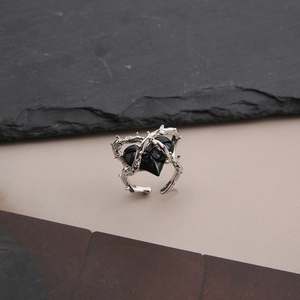 Macro detail of thorn-shaped silver ring featuring a black heart in punk aesthetic