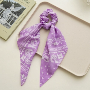 Detail of purple paisley silk scrunchie with long ribbons on a cream tray background