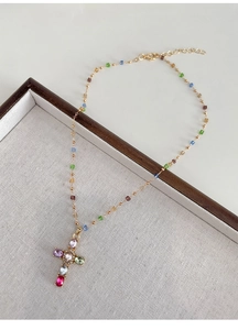 Gros plan d'un pendentif croix en zircon multicolore sur une fine chaîne dorée perlée
