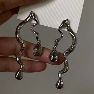 Macro view of liquid metal style wavy silver drop earrings on a display card