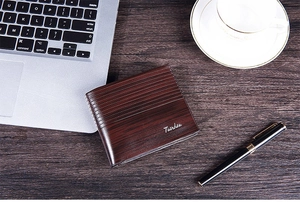Short brown bifold wallet with wood grain texture on an office desk with coffee and laptop