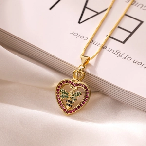 Detail of gold heart pendant with red gem and bee motif on white silk background